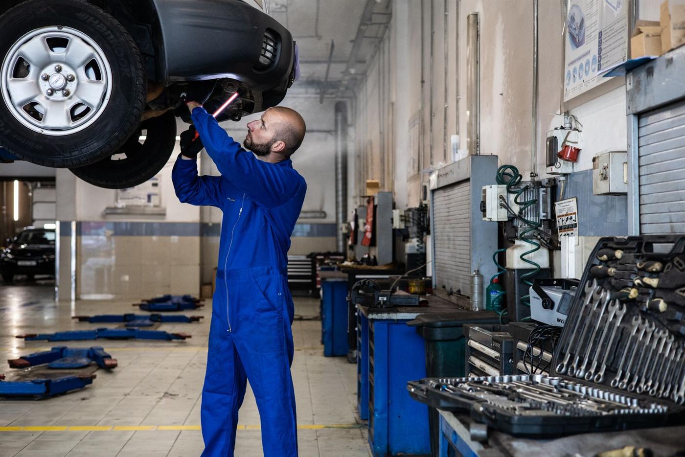 Mécanicien en bleu de travail sous un véhicule levé (photo d’illustration)